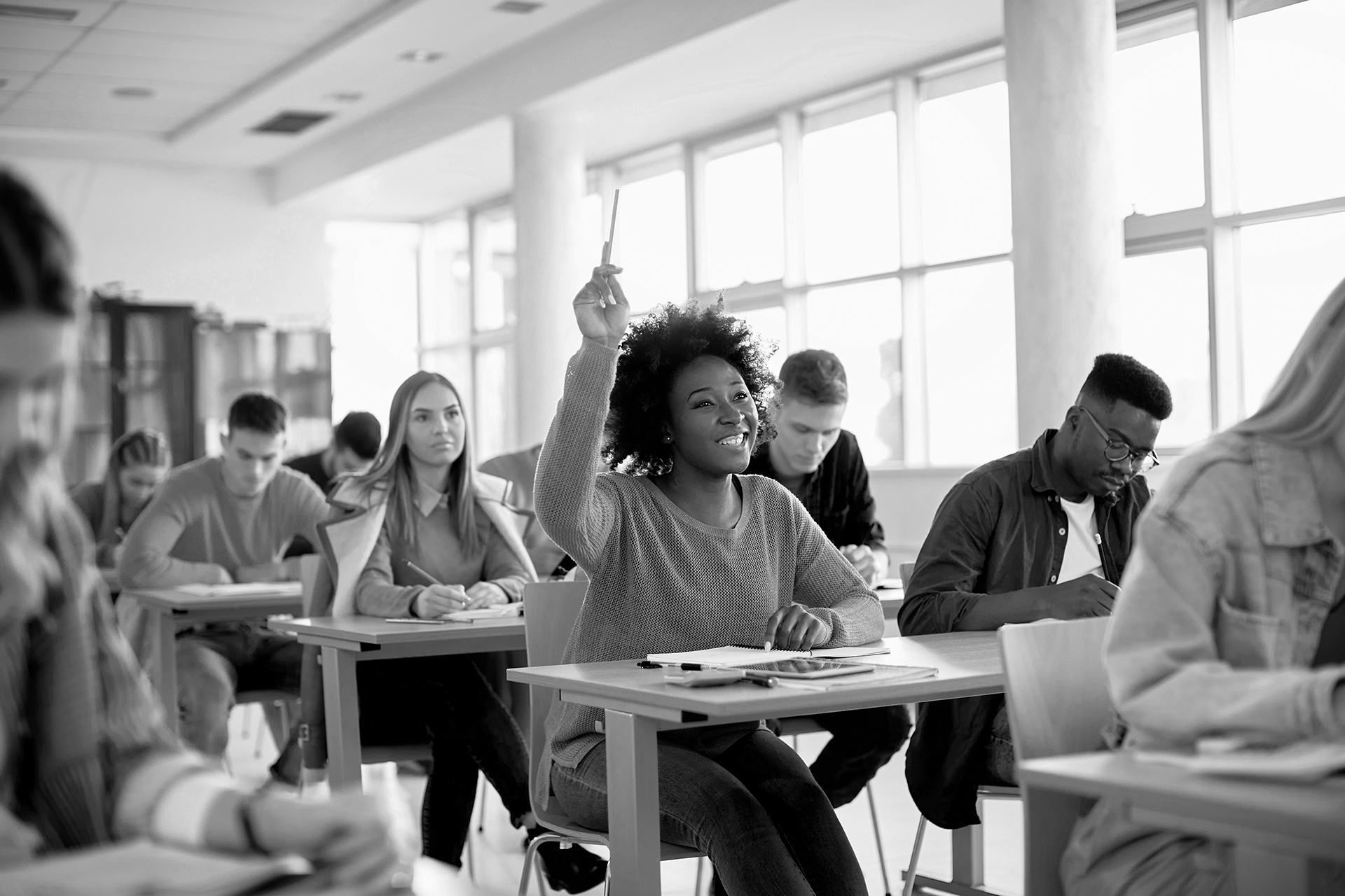 Happy black student raising arm to answer question while attendi