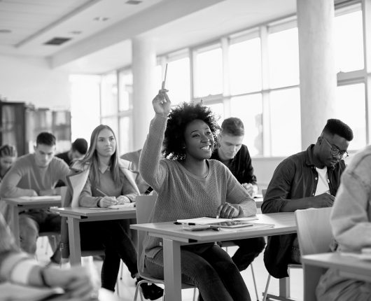 Happy black student raising arm to answer question while attendi